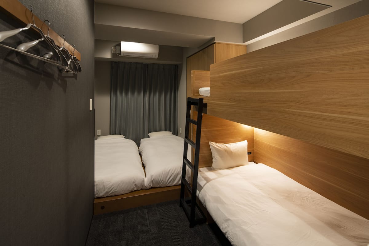 Habitación de hotel con dos camas, cabecera de madera, perchero y ventana con cortinas.