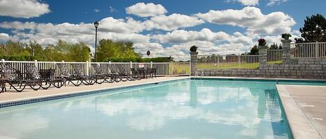 A rectangular swimming pool with a tiled edge, surrounded by a white fence and stone walls.