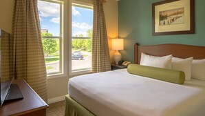 Una habitación de hotel con una cama, un escritorio, una lámpara y una ventana con cortinas.