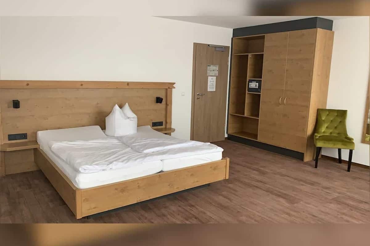 Ein Schlafzimmer mit einem hölzernen Bett, einem grünen Sessel und einem Kleiderschrank.