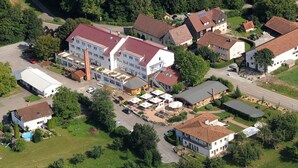 An aerial view of a residential area with multiple houses, a central building with a red roof, and a swimming pool. - Forsthof (Steinheim an der Murr)