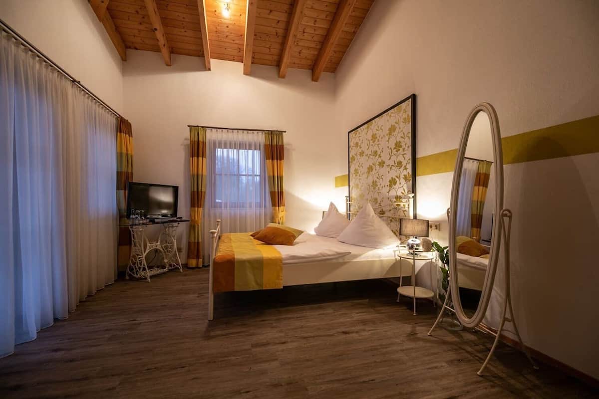 Ein Schlafzimmer mit einem Bett, einem Schreibtisch, einem Fernseher, einem Spiegel und einem Fenster mit Vorhängen.