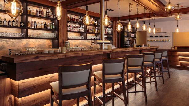 A bar area with wooden bar counters, hanging light fixtures, and shelves stocked with bottles. - Forsthof (Steinheim an der Murr)