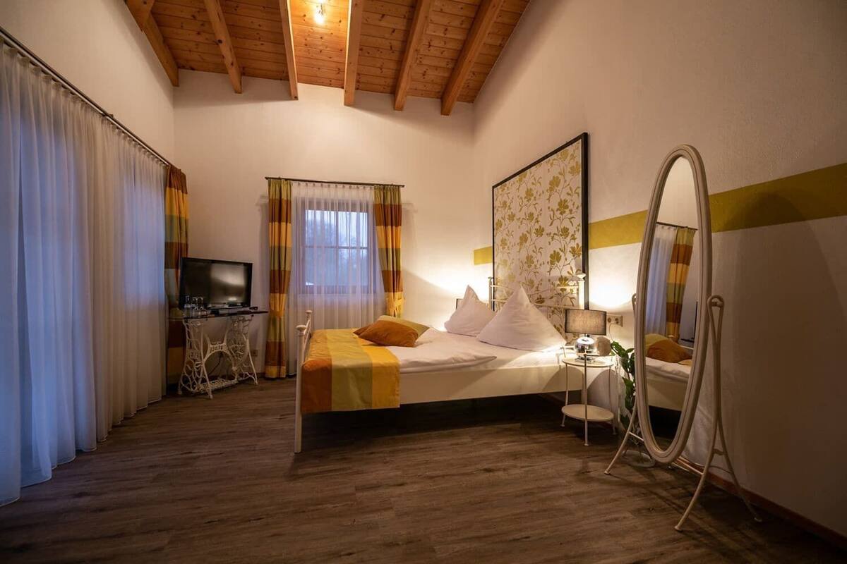 Ein Schlafzimmer mit einem Bett, einem Schreibtisch, einem Fernseher, einem Spiegel und einem Fenster mit Vorhängen.