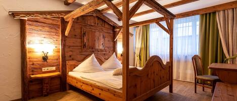 A wooden four-poster bed with a headboard, a wooden nightstand, and a wall-mounted light fixture.