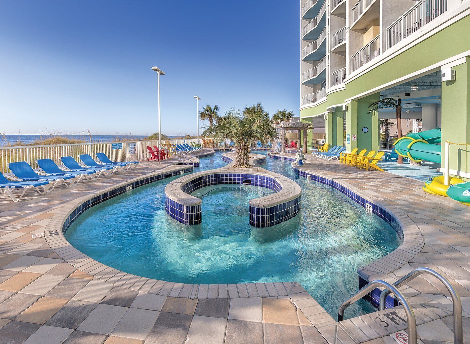 A pool area with a hot tub, lounge chairs, and a view of the ocean.