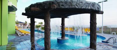 A pool area with a stone structure, water jets, and a tiled floor.