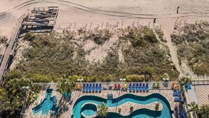 A beach resort with a swimming pool, sun loungers, and a boardwalk leading to the beach. - Cherry Grove Beach Resort best in SC. (North Myrtle Beach)