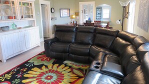 A living room with a black leather sectional sofa, a colorful floral rug, and a white cabinet with glass doors.