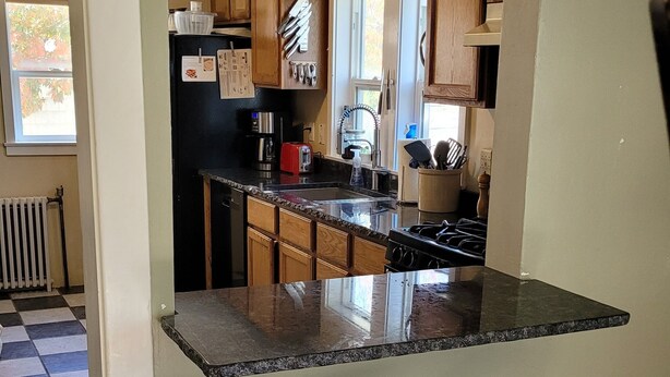 A kitchen with wooden cabinets, a black refrigerator, a red toaster, and a black countertop with two stools.