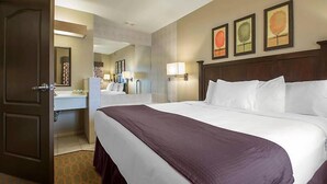 A hotel room with a large bed, a bathroom with a mirror, and three framed pictures on the wall.