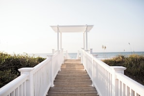 A wooden boardwalk leading to a white pergola with railings, overlooking a beach. - Oceanside Interior Home,Private Pool,Golf Cart,Beach Access,in Spinnaker's Reach (Emerald Isle)