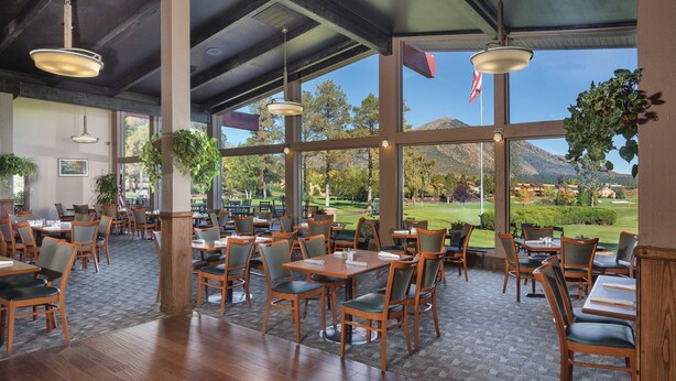 Un vaste espace de restauration intérieur, doté de tables et de chaises en bois, et de grandes fenêtres offrant une vue sur un terrain de golf et les montagnes.
