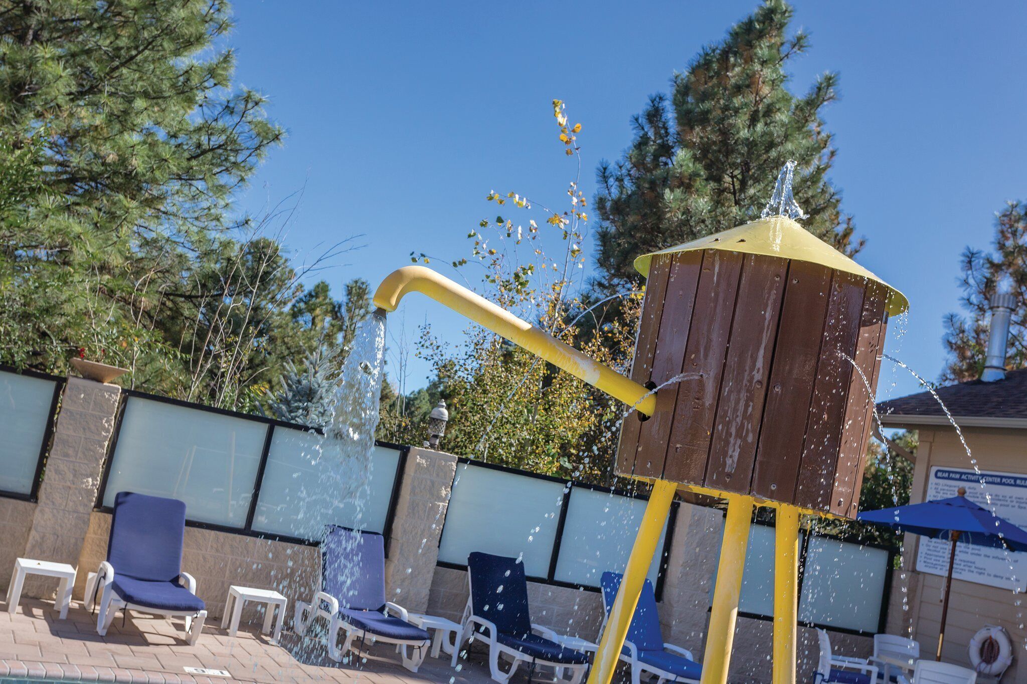 Un élément décoratif aquatique composé d’une structure jaune et brune, entouré de chaises longues et d’une piscine.