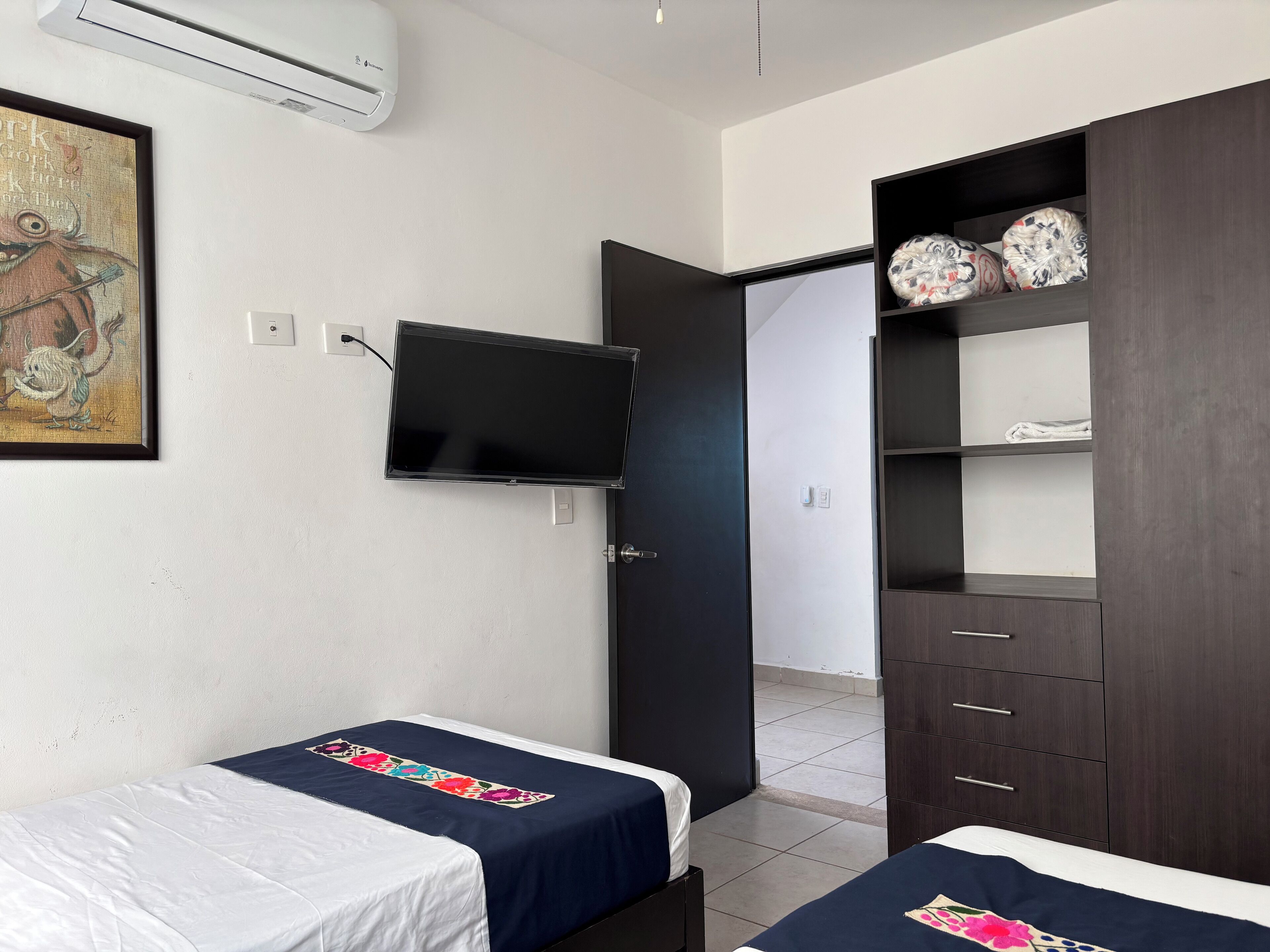 Une chambre d’hôtel avec deux lits, un téléviseur fixé au mur, une armoire et un tableau.
