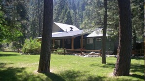 A cabin with a sloped roof, surrounded by a wooden deck and a grassy yard. - The Last Resort Lodge (New Meadows)
