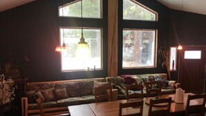 A cozy room with a wooden dining table, chairs, and a sofa. There are large windows allowing natural light. - The Last Resort Lodge (New Meadows)
