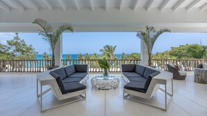 A spacious balcony with a white ceiling, two black sofas, a round table with a vase, and a view of the ocean. - Luxury Contemporary Villa with Sea View & Private Pool – Las Terrenas STARLINK (Las Terrenas)