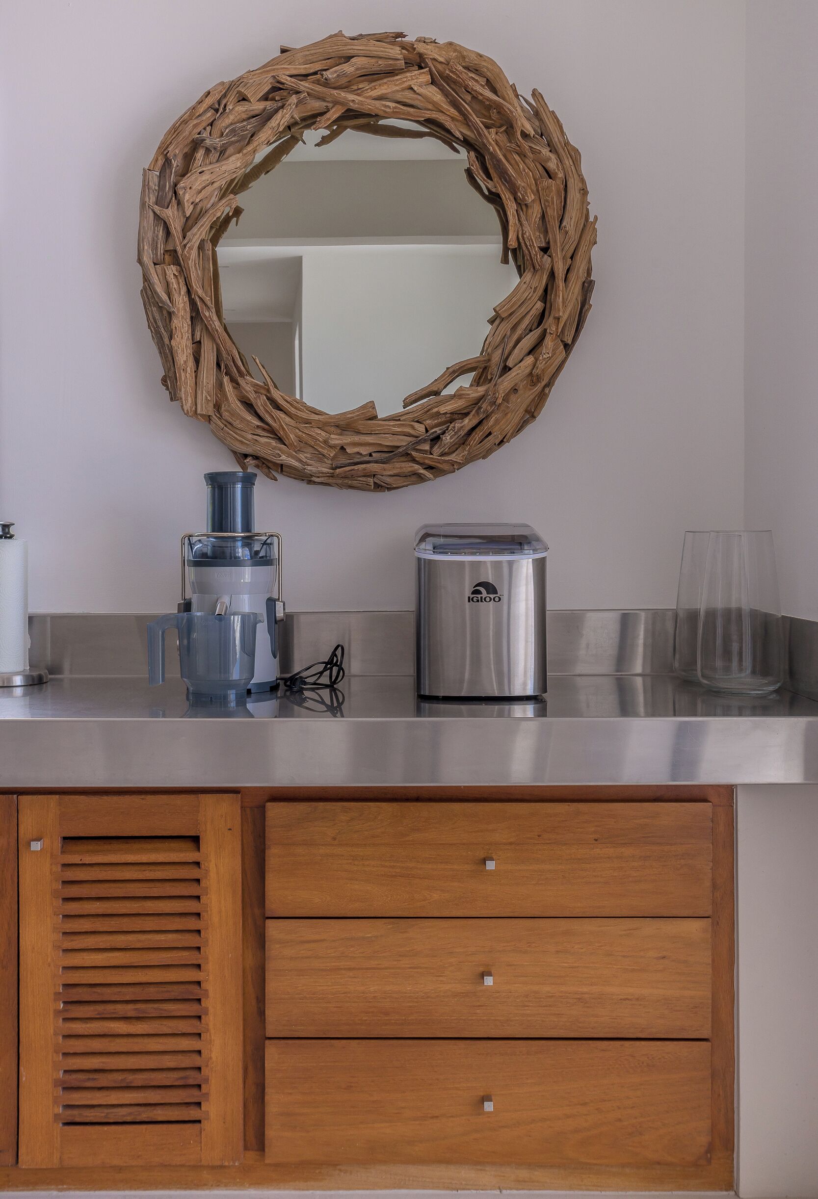 A kitchen with a wooden cabinet, a stainless steel countertop, a blender, a toaster, and a glass.