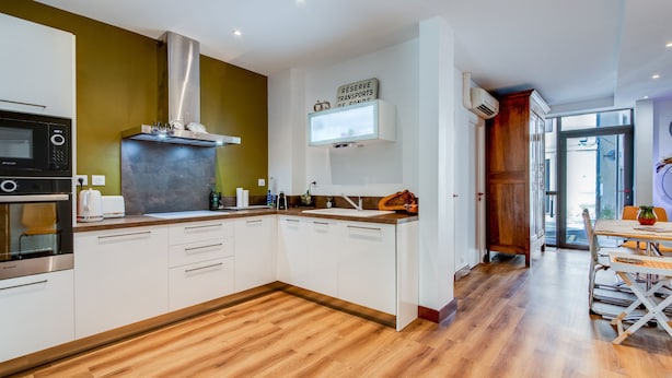 Una cucina moderna con mobili bianchi, una cappa in acciaio inossidabile e un pavimento in legno.