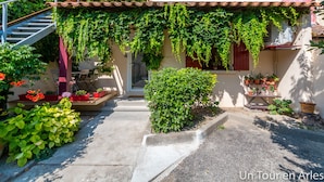 Un cortile con una scala che conduce a una porta, circondato da vegetazione rigogliosa e piante in vaso.