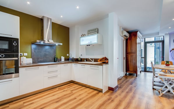 A modern kitchen with white cabinets, a stainless steel range hood, and a wooden floor.