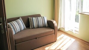 Um sofá marrom com almofadas listradas em frente a uma parede verde-clara, posicionado perto de uma janela com cortinas translúcidas.