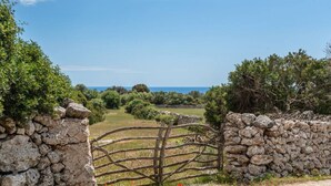 A rustic stone gate with a wooden fence leading to a lush green landscape and a clear view of the sea. - Binicalaf · ❤️Finca Binicalaf Vell (Maó)