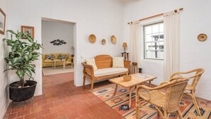 A cozy living room with a wooden sofa, a wicker chair, a small table, and a potted plant. - Binicalaf · ❤️Finca Binicalaf Vell (Maó)