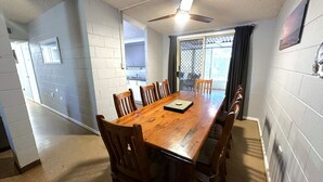 A dining area with a wooden table and chairs, a ceiling fan, and a view through a window with a metal screen. - 15 Grenadier Street - family home with all that you need (EXMOUTH)