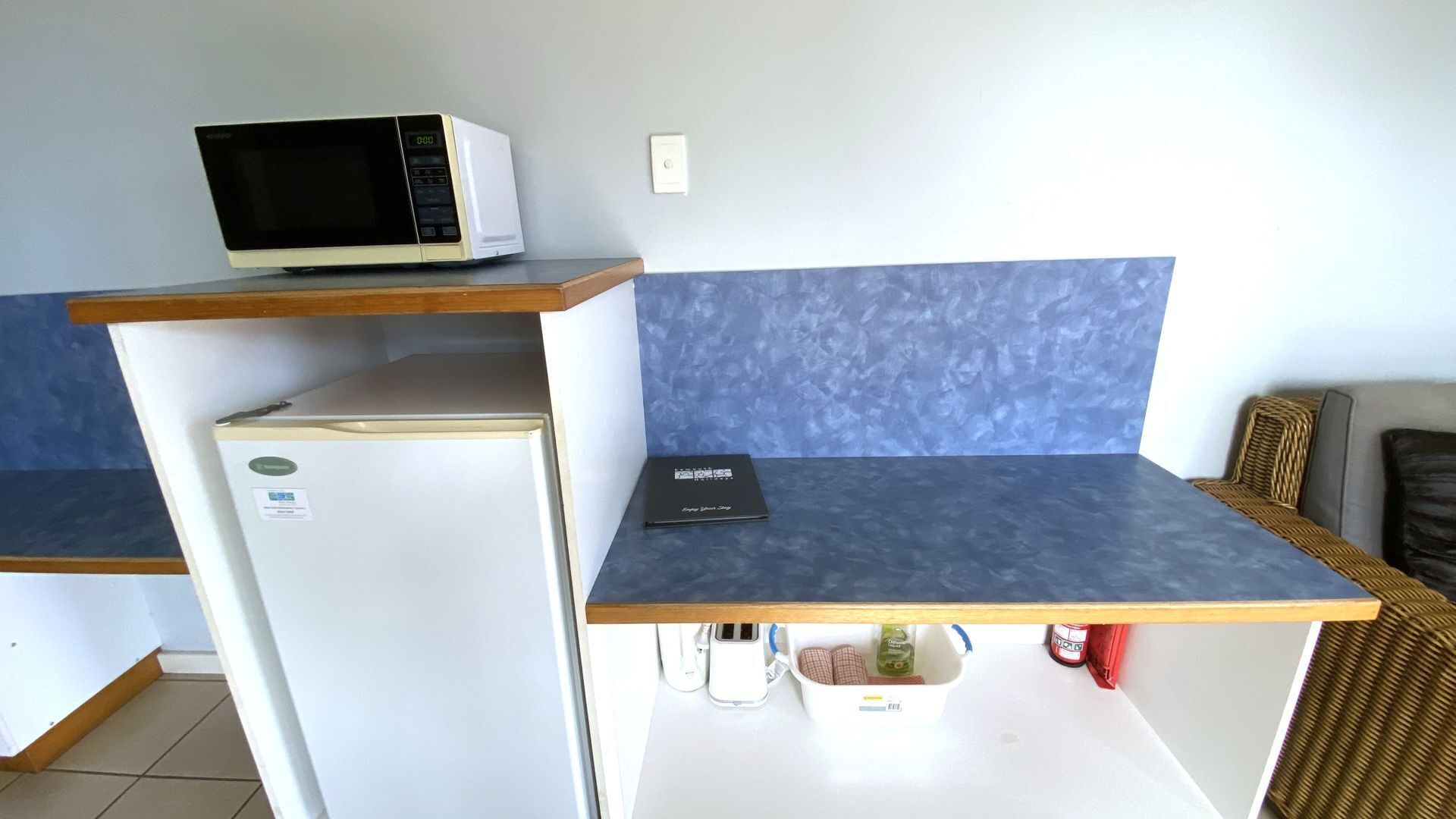 A compact kitchenette with a microwave, a small refrigerator, and a countertop with a book.