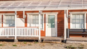 Une rangée de cabanes en bois, dotées de balustrades blanches et de portes numérotées, avec un sol en gravier et un toit en métal.