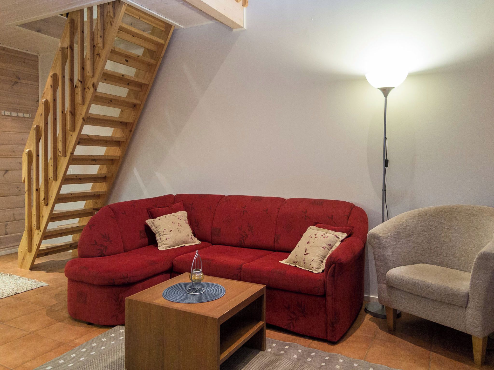 Una sala de estar con un sofá rojo, un sillón beige, una mesa de centro de madera y una lámpara de pie.