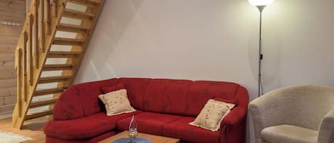 A living room with a red sofa, a beige armchair, a wooden coffee table, and a floor lamp.