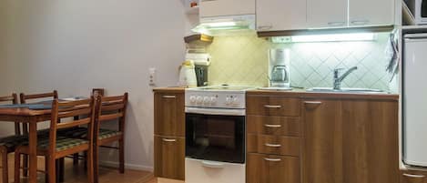 A compact kitchen with a stove, oven, and a coffee maker. There is a dining table with chairs and a small rug on the floor.