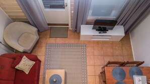 Un espace de vie compact comprenant un canapé rouge, une table basse en bois, une table à manger avec des sets de table bleus, un téléviseur posé sur un meuble blanc et une porte avec une fenêtre.