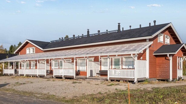 Une rangée de cabanes en bois peintes en rouge, dotées de balustrades blanches, et numérotées de 10 à 19, ainsi qu’une allée couverte.