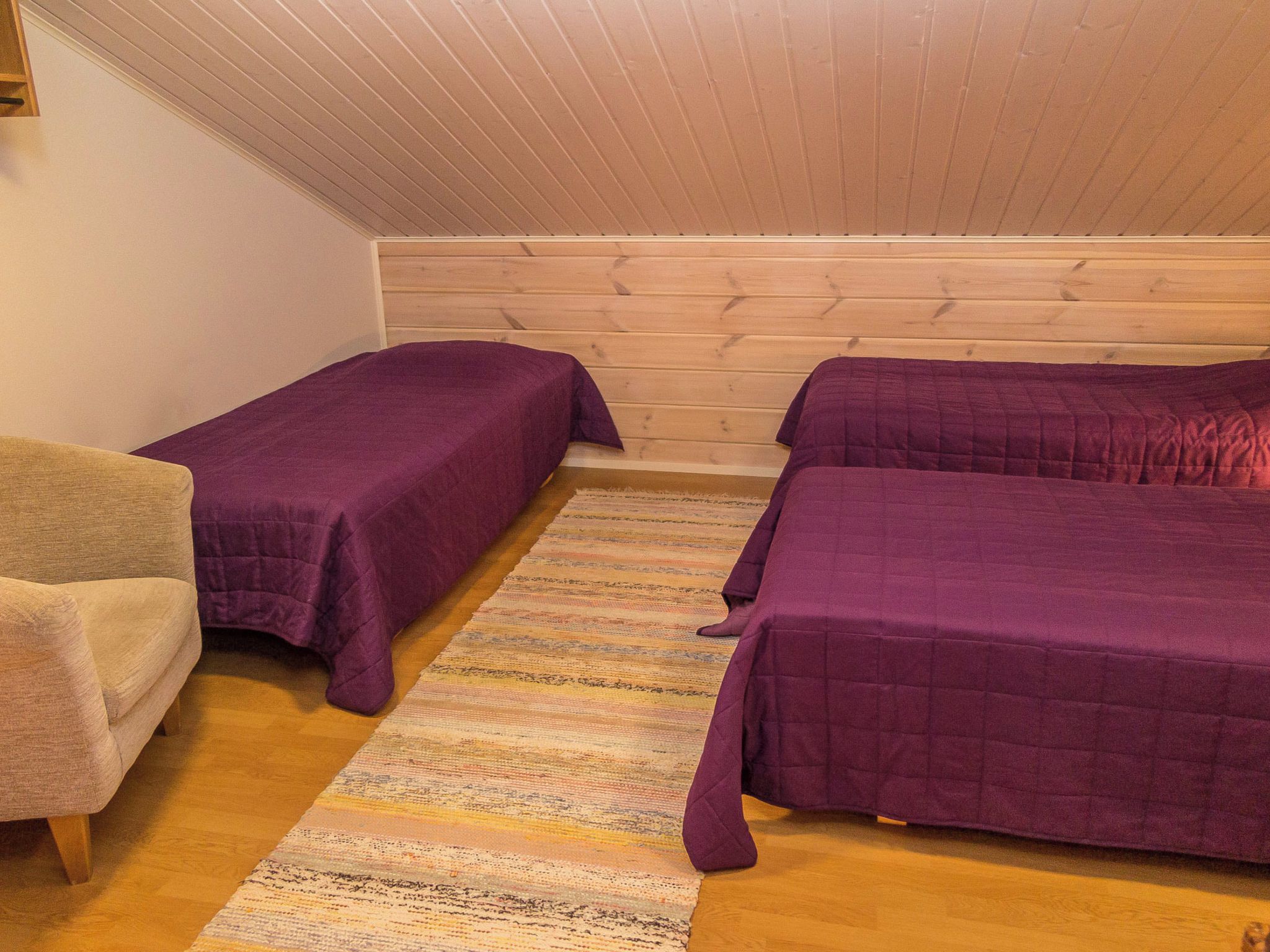 Una habitación con dos camas, una silla y techo de madera.