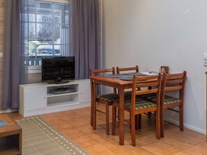 A dining area with a wooden table and chairs, a television on a white cabinet, and a window with curtains.