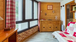 A bedroom with a wooden dresser, a bed with a quilt, a window with curtains, and a wall-mounted shelf. - Belleville Caron 3 - 624 by Interhome (Les Menuires)