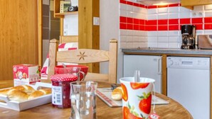 A kitchen with a wooden chair, a table with bread, a coffee maker, and a dishwasher. - Belleville Caron 3 - 624 by Interhome (Les Menuires)