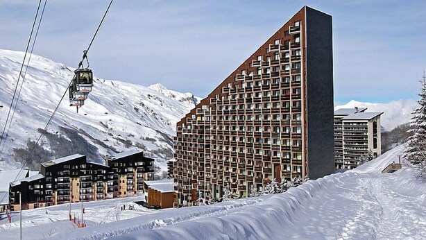 A modern ski resort with a large building featuring a grid-like facade, a ski lift, and snow-covered mountains in the background. - Belleville Caron 3 - 624 by Interhome (Les Menuires)