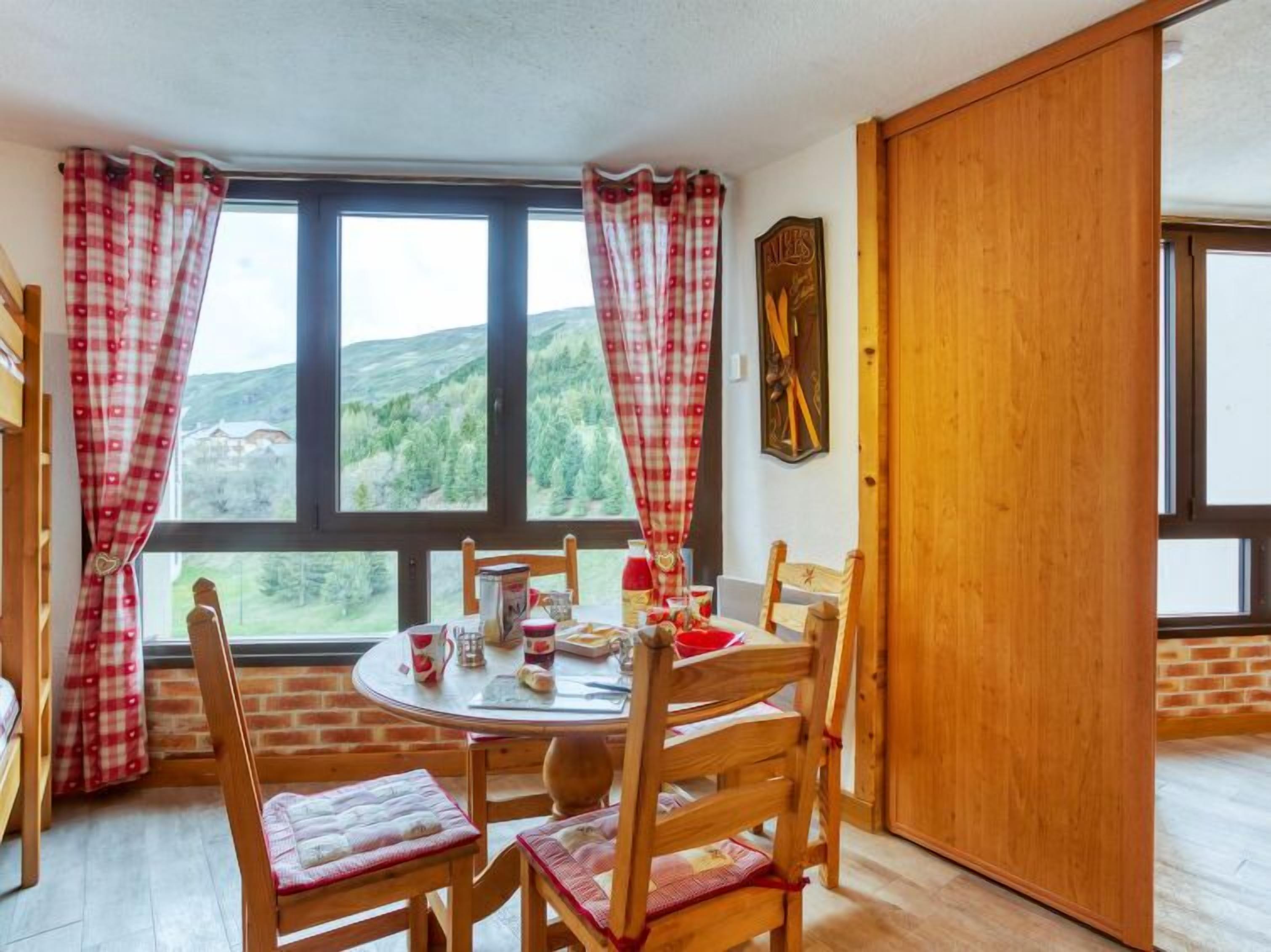 Un coin repas accueillant avec une table ronde, des chaises en bois et une vue sur un paysage montagneux grâce à de grandes fenêtres.