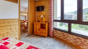 A cozy room with a wooden bunk bed, a wooden desk with a lamp, a television mounted on the wall, and a large window offering a view of the outside. - Belleville Caron 3 - 624 by Interhome (Les Menuires)