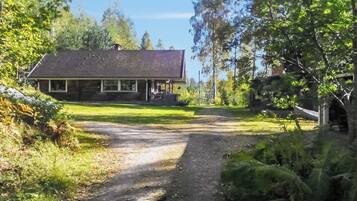 Une maison avec un porche, entourée d’arbres et accessible par un chemin de terre.