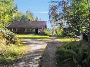Ett hus med en veranda, omgivet av träd och en grusgång som leder fram till det.