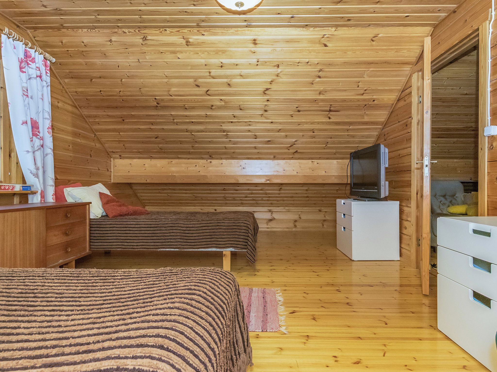 Una cabaña de madera con una cama en el altillo, un televisor y un aparador.