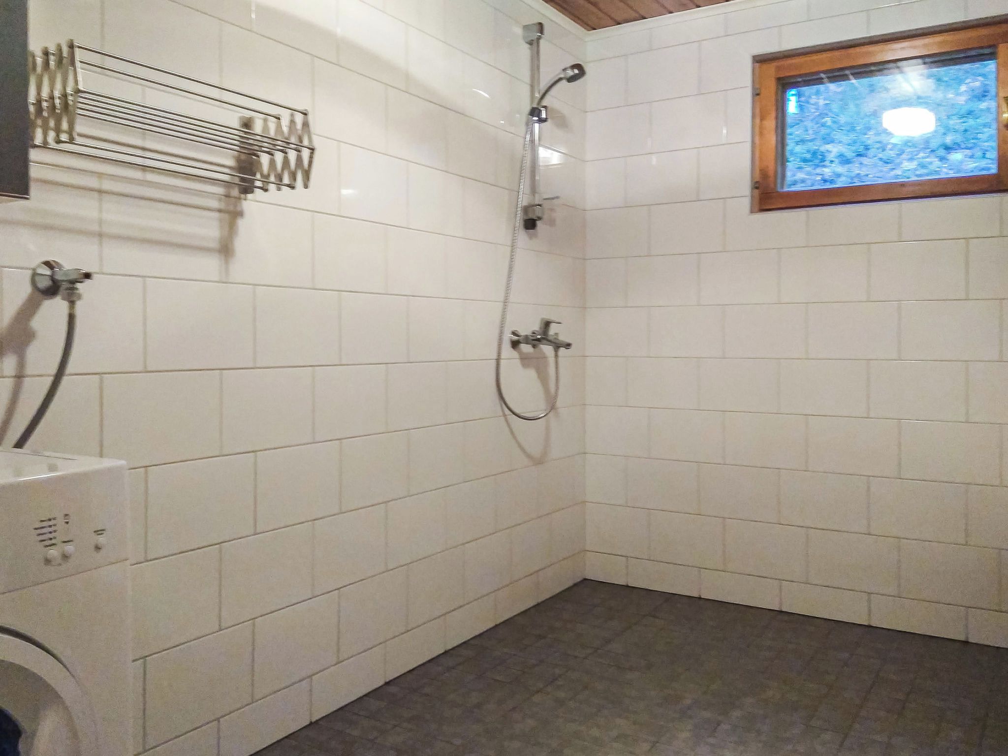 Ein Badezimmer mit weißen Fliesen, einer Dusche inklusive Handbrause und einem Fenster mit Blick zum Himmel.