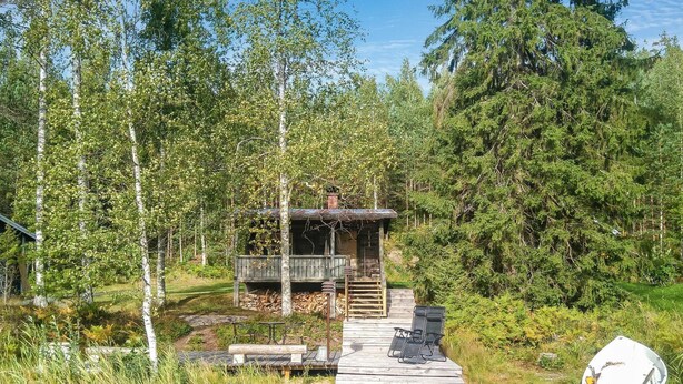 A rustic cabin with a wooden deck leading to a small porch, surrounded by dense forest and a calm body of water. - Saarijärvi by Interhome (Sulkava)