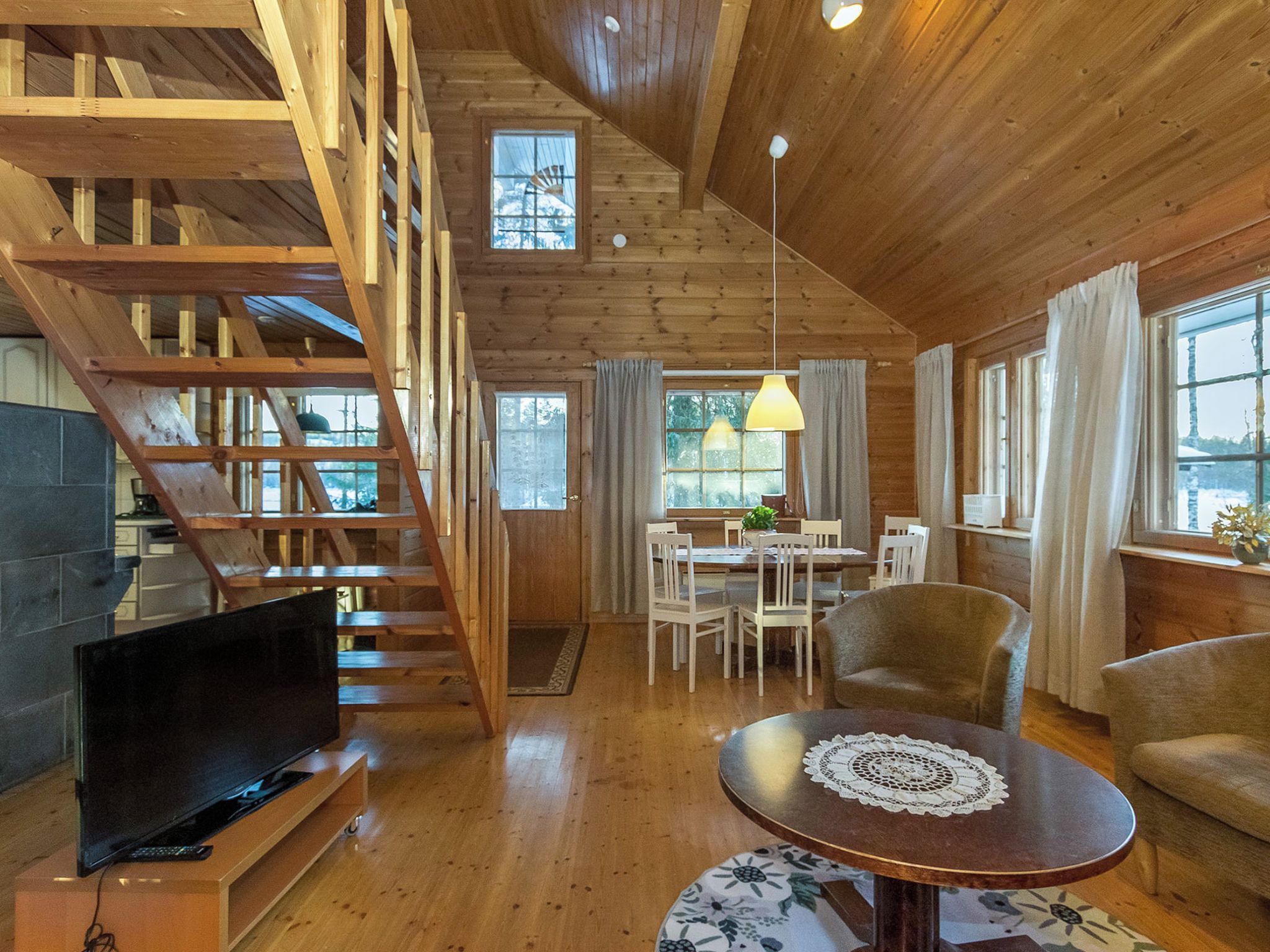 A wooden interior with a staircase, a dining area, and a television.